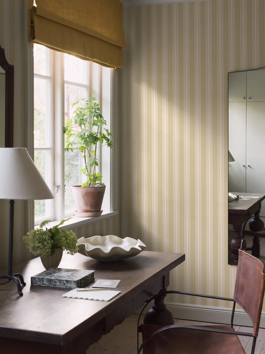 This Gunnebo wallpaper showcases cream-colored stripes set against a soft yellow background and evokes the charm of Gustavian interiors.