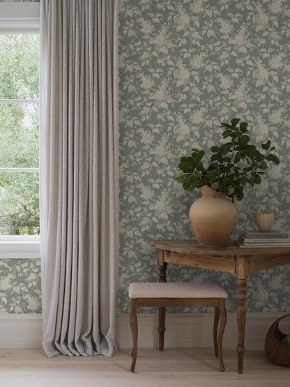 This Syren wallpaper in green features a delicate silhouette pattern of lilac branches and small roses, surface printed in beige and cream on a powdery jade background.