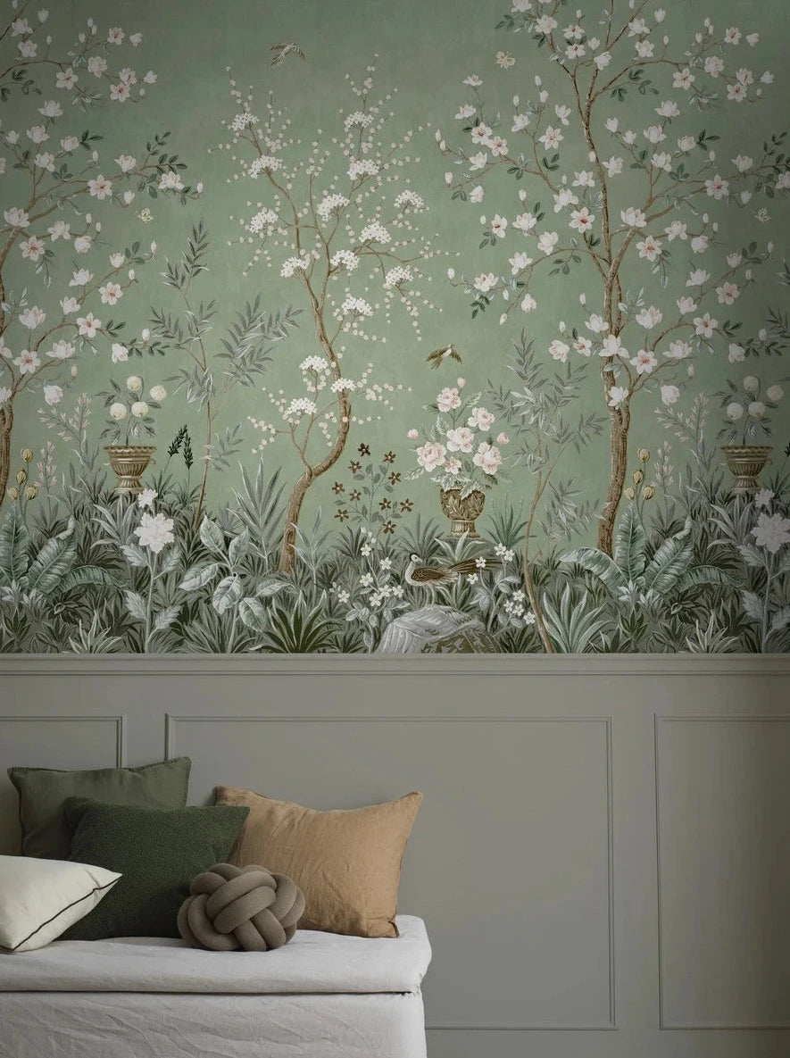 The green wallpaper Magnolia Garden is adorned with a lush, hand-painted pattern in classic chinoiserie style, featuring blooming trees, grand flower urns, and beautiful birds.