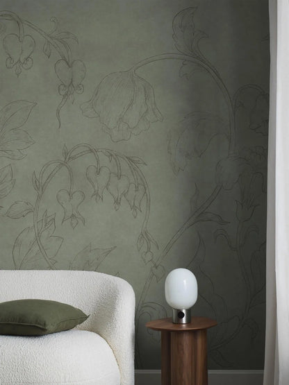 The green wallpaper Burning Heart is adorned with an airy, large-scale floral pattern of delicate bellflowers and bleeding hearts climbing towards the ceiling. 